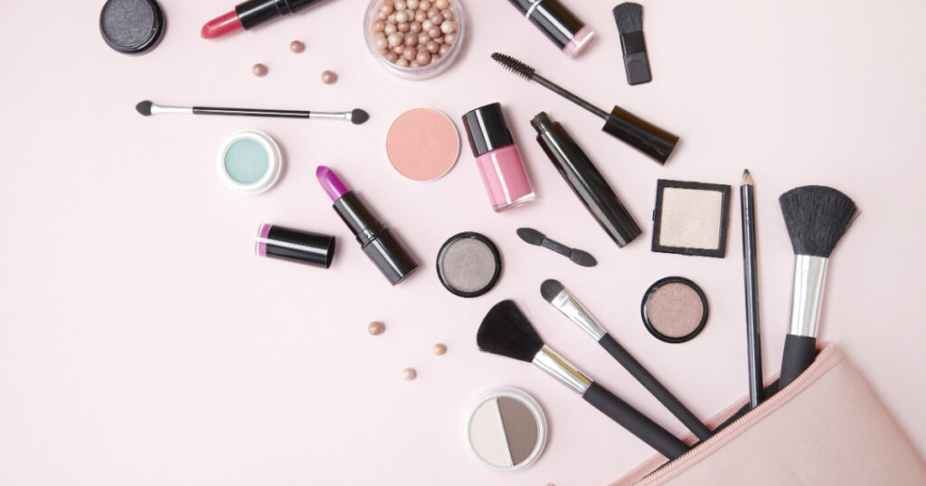 A pink makeup bag with cosmetic beauty products spilling out on to a pastel colored background, with empty space at side
