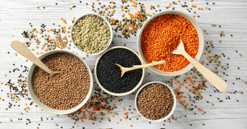 Bowls with different types of lentils on wooden table