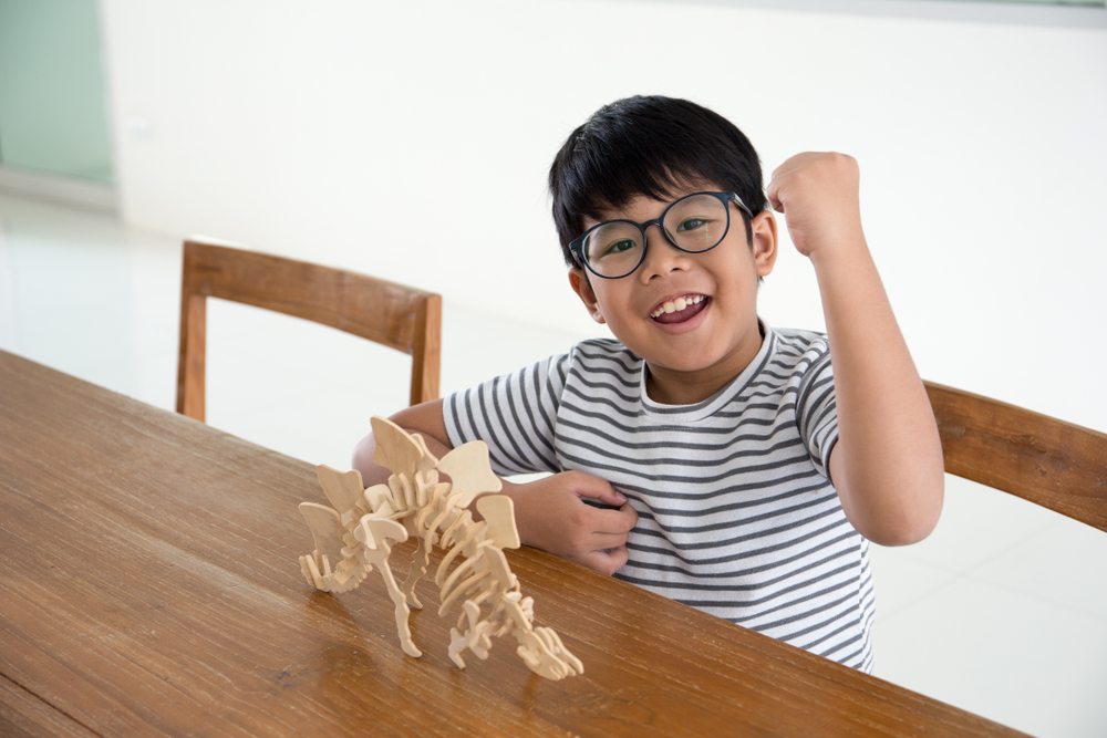 Happy Asian kid proud to finish making a 3D dinosour wood puzzle toy
