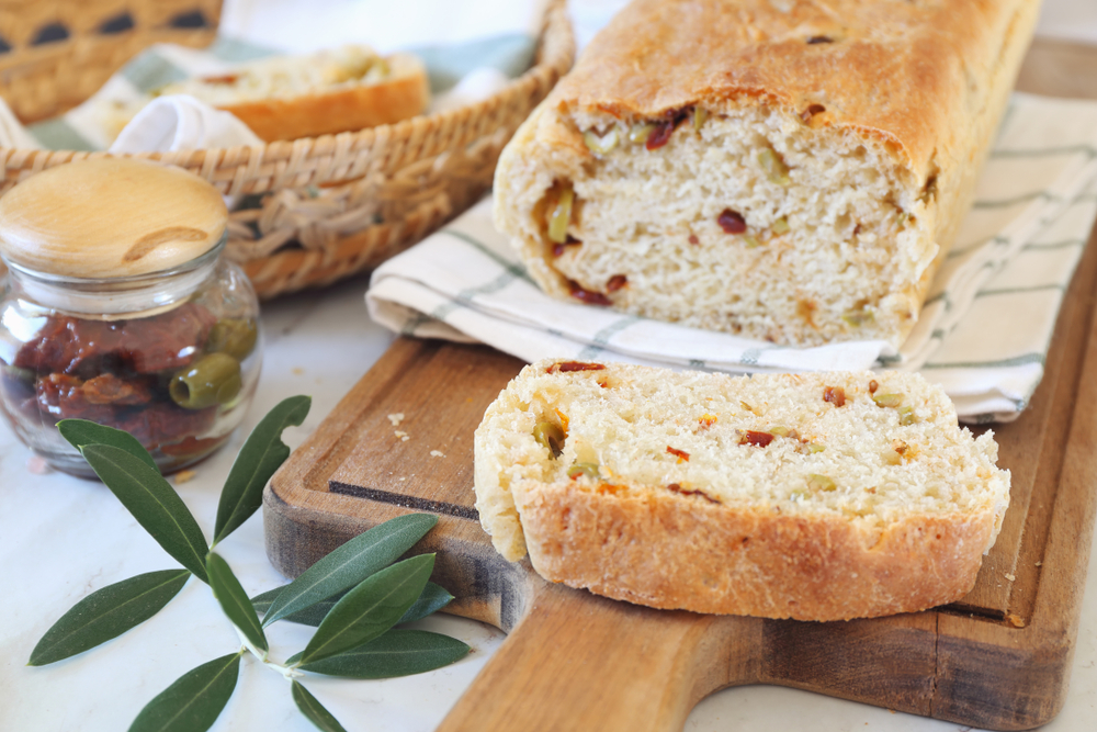 Mediterranean cuisine. Homemade sourdough bread with dried tomatoes and olives on wooden chopping board