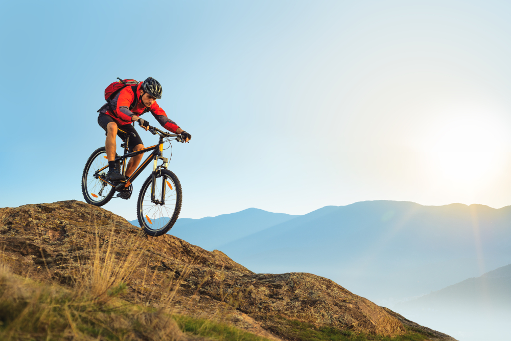 Cyclist in Red Jacket Riding the Bike in the Beautiful Mountains Down the Rock on the Sunrise Sky Background. Extreme Sport and Enduro Biking Concept.