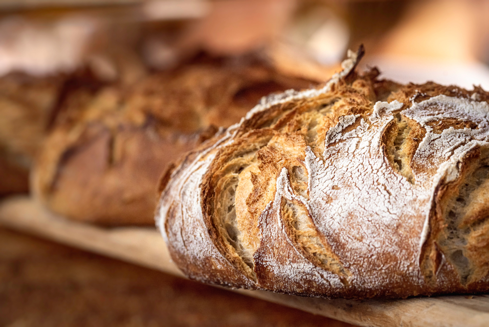 Round bread close-up. Freshly baked sourdough bread with a golden crust on bakery shelves. Baker shop context with delicious bread. Pastry items.