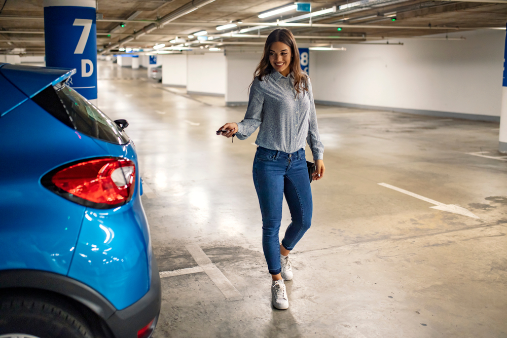 Woman in a parking garage, unlocking in her car. Woman activating her car alarm in an underground parking garage as she walks away. Business woman walking with car keys in the underground parking