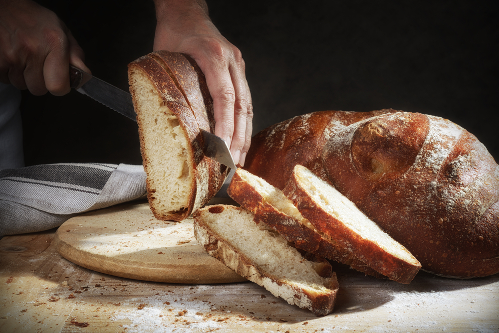 Hands cut homemade bread with organic stone ground flour.