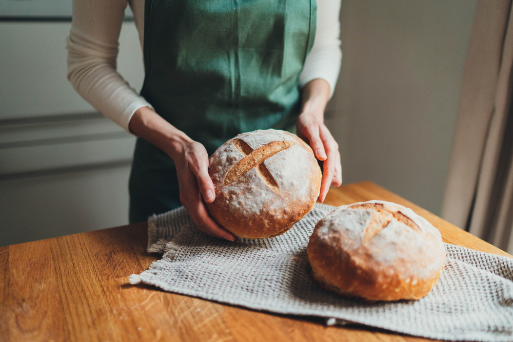 Woman in green linen apron holding homemade sourdough bread, Cooking at home, Homemade country bread loaf