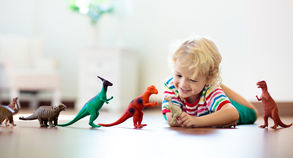 Child playing with colorful toy dinosaurs. Educational toys for kids. Little boy learning fossils and reptiles. Children play with dinosaur toys. Evolution and paleontology game for young kid.