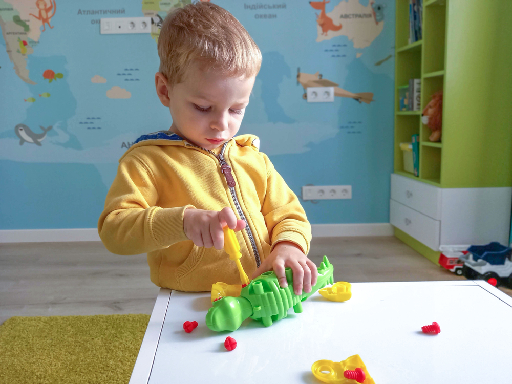 A little boy collects a toy dinosaur from the details of a children's construction set.