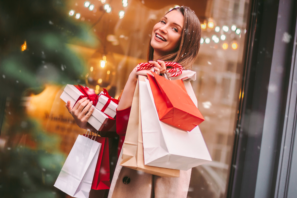 Beautiful happy girl hold shopping bags and gift boxes in hands and smile on city street. Young attractive cheerful woman with paper bags and present box after Christmas shopping in mall. Winter sale