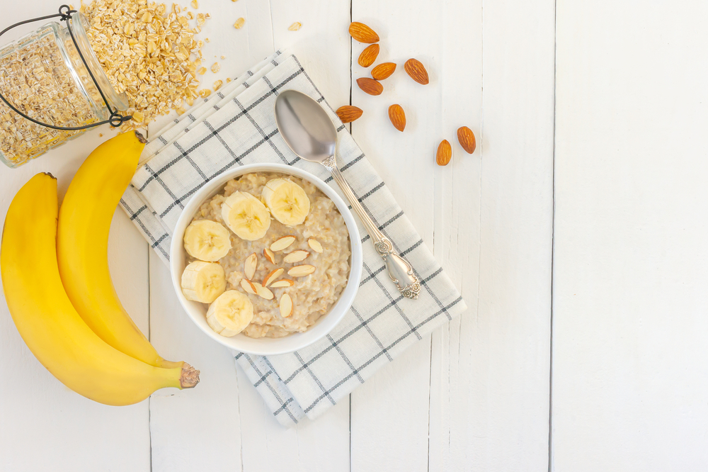 Top view of Bowl of oat flakes with sliced banana close-up on wooden table.