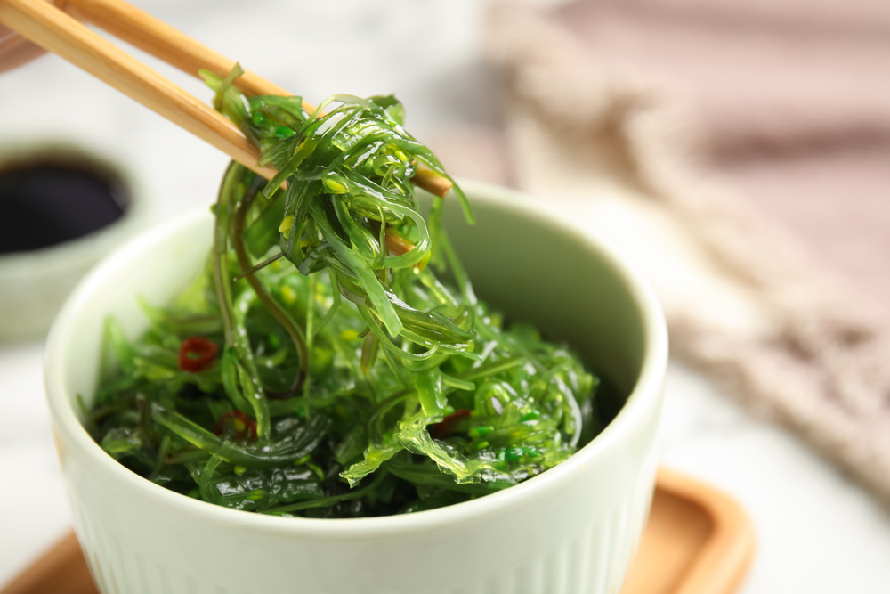 Chopsticks with Japanese seaweed salad in bowl on table, closeup
