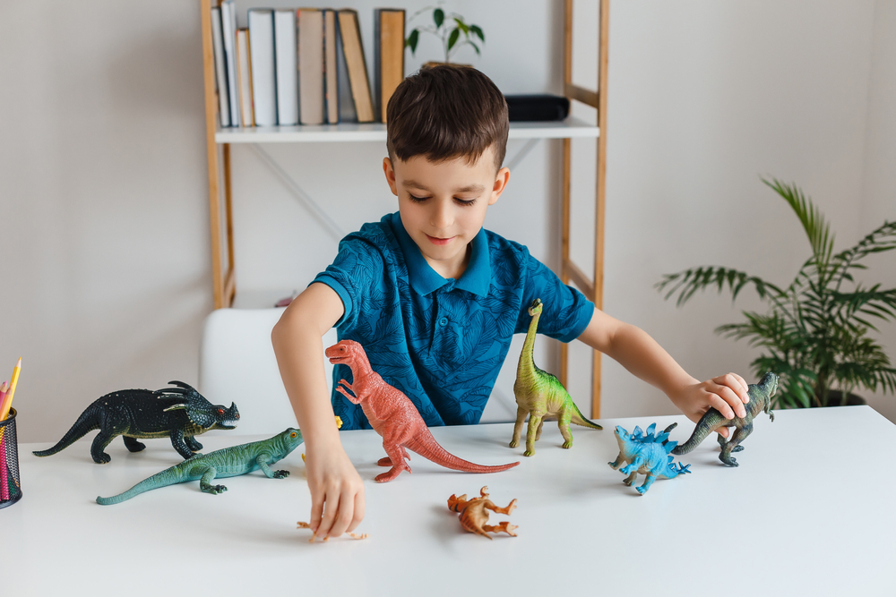 Focused kid playing with dinosaurs at home. Boy learning paleontology by dino toys at leisure. Concept of clever child and early education