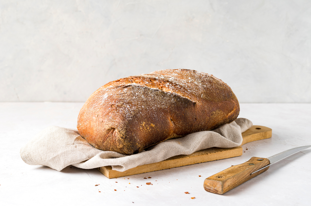 Loaf of bread, and knife, on delicate background. Front view. Copy space.