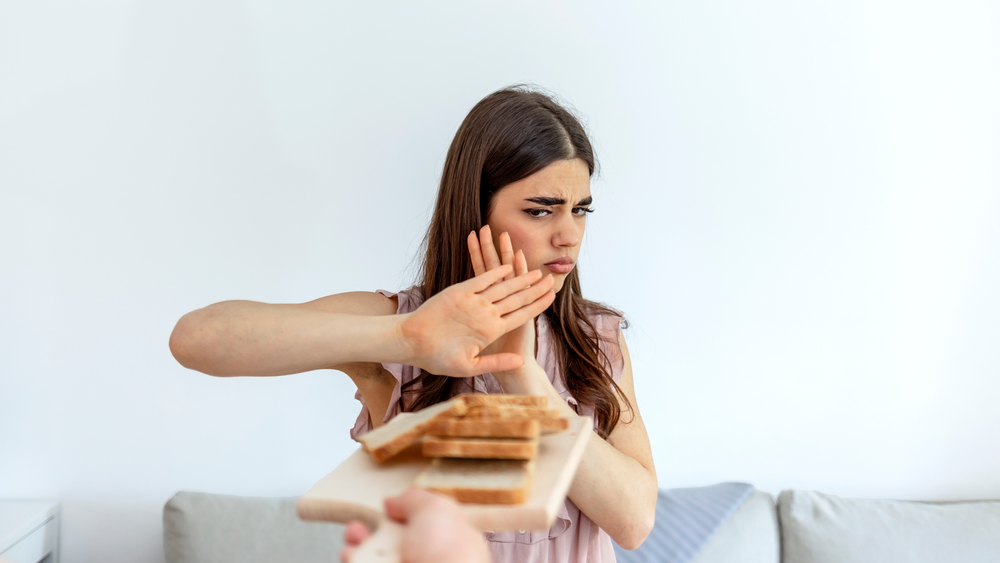 Cropped shot of a young woman on a gluten free diet is saying no thanks to white bread. Woman refusing to eat white bread. Gluten intolerance concept. Health care and medicine concept. Copy space.
