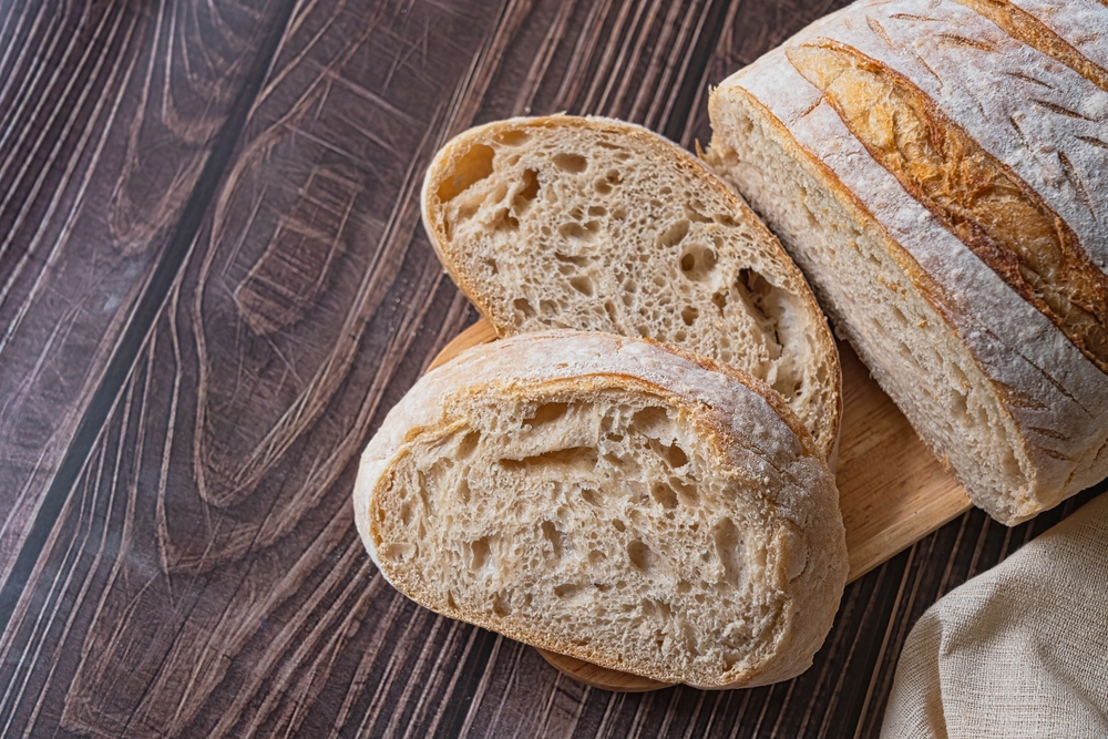 Sourdough bread loaf, artisan bread cut into pieces on a wooden plate on a wooden table, top view, close up