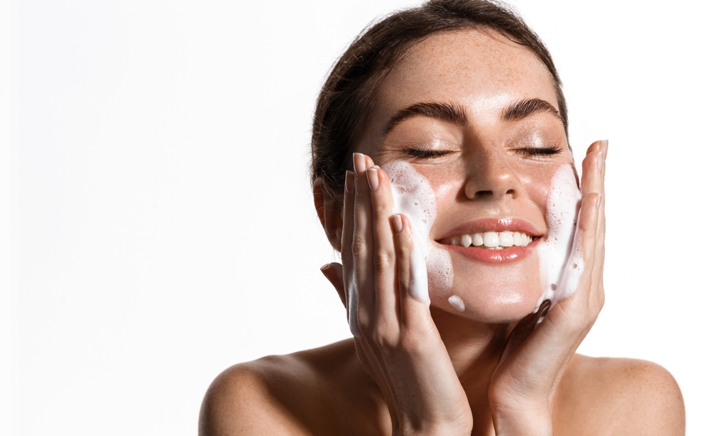 Portrait of cheerful laughing woman applying cleansing foam for washing face. Lovely brunette with attractive appearance. Skincare spa relax concept. Isolated on white background