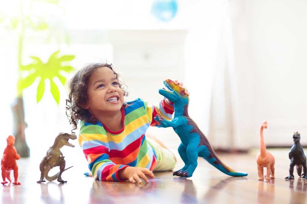 Child playing with colorful toy dinosaurs. Educational toys for kids. Little boy learning fossils and reptiles. Children play with dinosaur toys. Evolution and paleontology game for young kid.