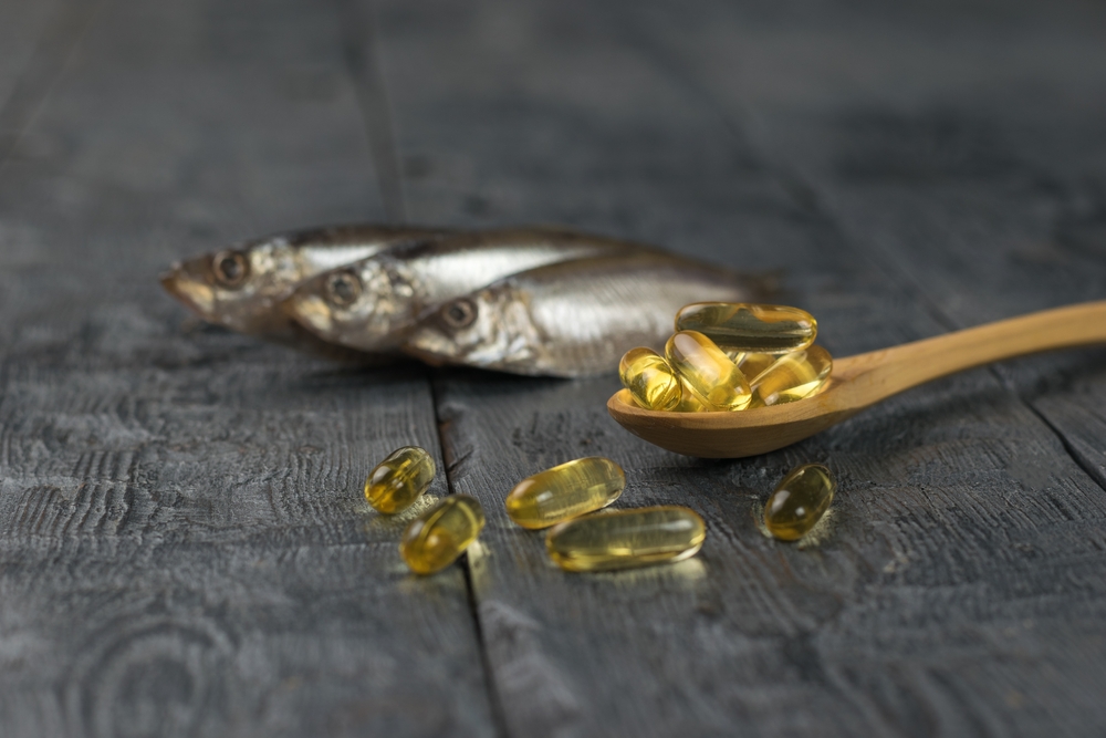 Wooden spoon with fish oil capsules on the background of three fish on a wooden table. Biologically active additive.