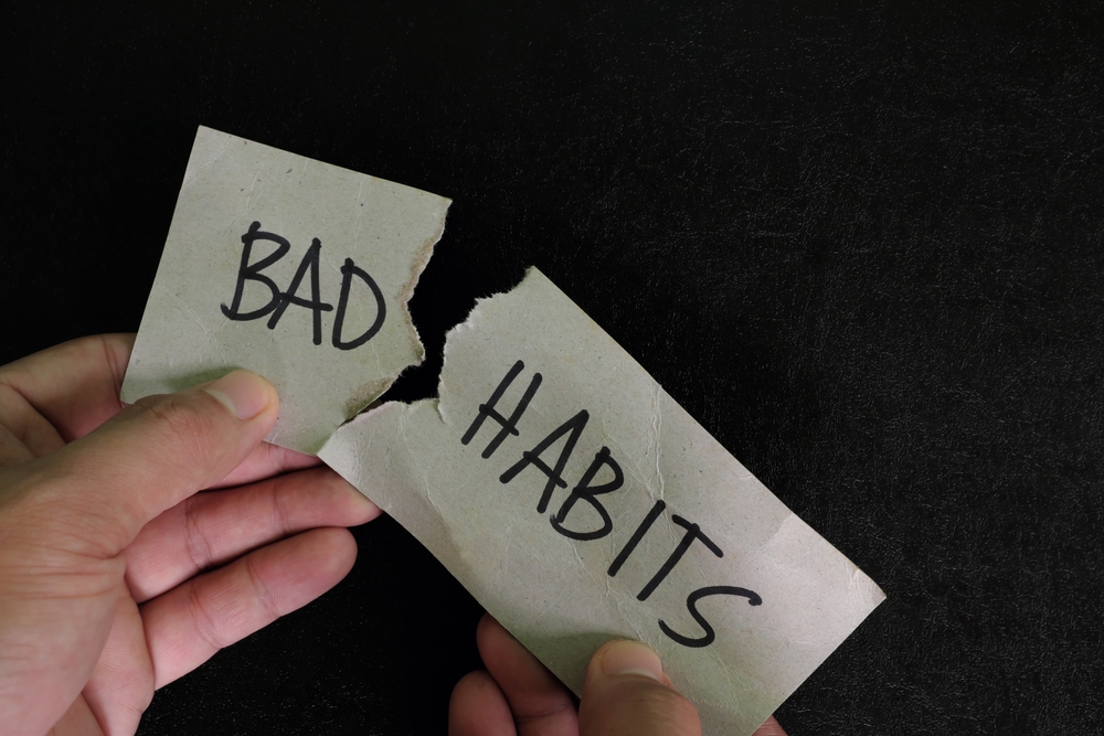 Breaking bad habits concept. Human hand tear a paper with word bad habit in dark black background.

