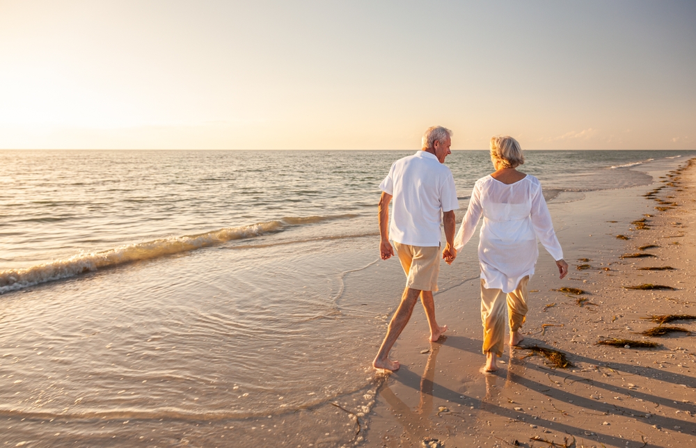 Happy senior man and woman old retired couple walking and holding hands on a beach at sunset, s3niorlife