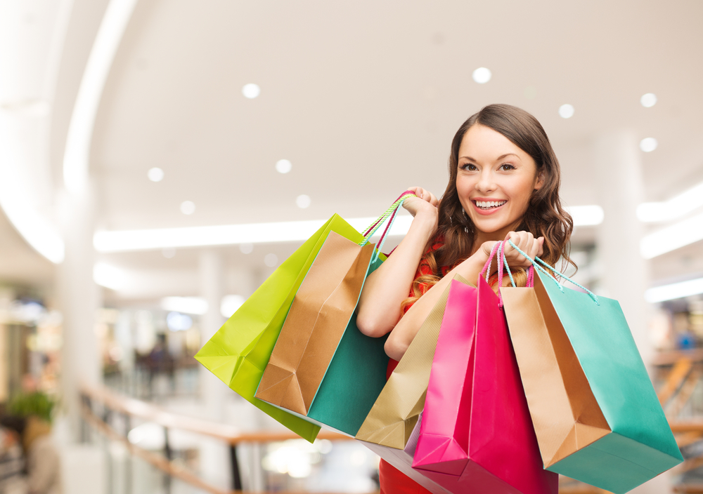 happiness, consumerism, sale and people concept - smiling young woman with shopping bags over mall background