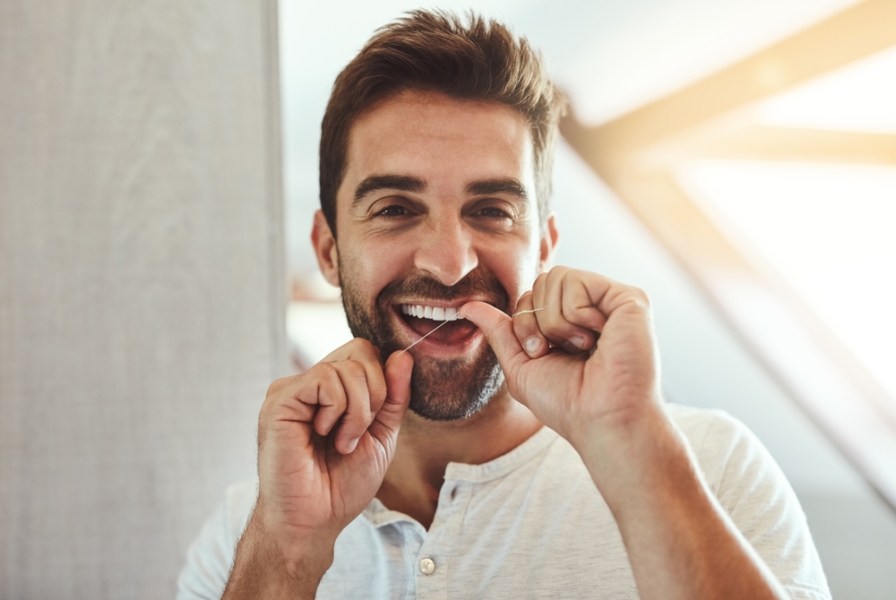 Dental floss, teeth and smile with portrait of man in bathroom for cleaning, morning and oral hygiene. Happy, cosmetics and health with face of person flossing at home for self care, breath and mouth
