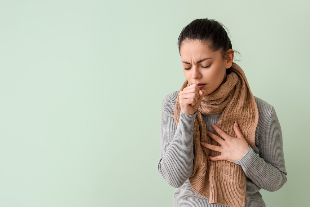 Ill young woman coughing on green background
