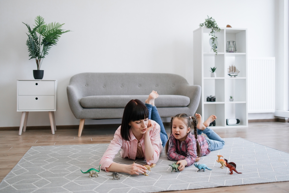 Playful tween girl with animal toy having fun with brunette woman in living room of spacious apartment. Mindful mother encouraging scientific exploration while keeping daughter entertained indoors.