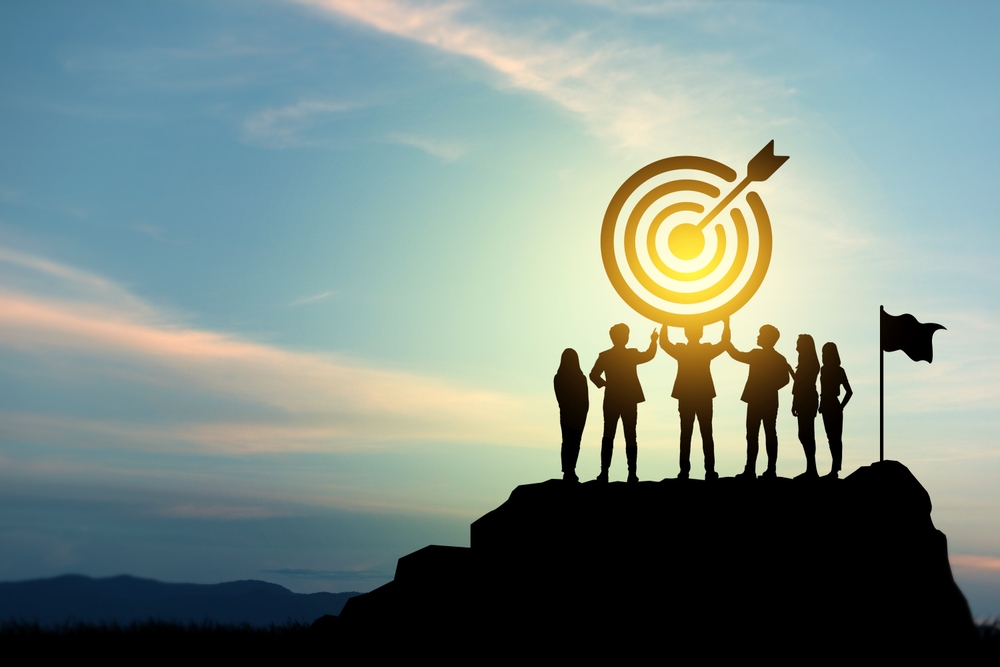 Goal setting towards planning for the future. Silhouettes of group businessmen holding target boards with flags planted on a mountain. Concept of a clear planning process and teamwork.