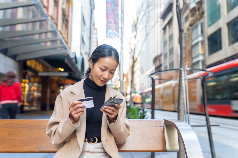 Asian woman using mobile phone with credit card booking hotel or online shopping during travel in Australia. Attractive girl enjoy outdoor lifestyle travel and shopping in the city on holiday vacation