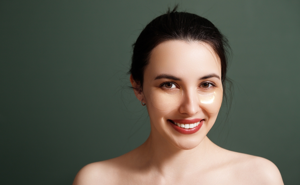 Under eye masks for puffiness, wrinkles, dark circles. A young beautiful smiling woman with cosmetic patches on her eyes. Cosmetic procedures skin care around the eyes. Perfect healthy facial skin