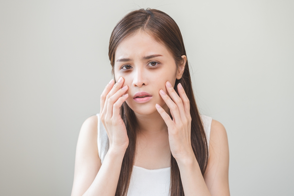 Bored, insomnia asian young woman, girl looking at camera, hand touching under eyes with problem of black circles or panda puffy, swollen and wrinkle on face. Sleepless, sleepy healthcare person.