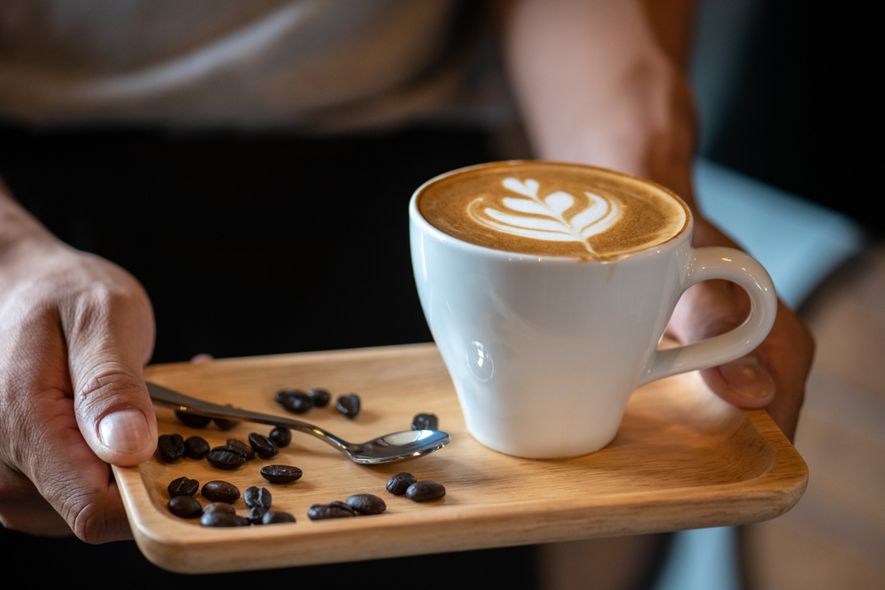 White ceramic cups of cappuccino with latte art Barista make coffee by pouring spills hot milk cream on black coffee. Barista serve holding cup of hot latte and coffee beans on wooden table cafe shop

