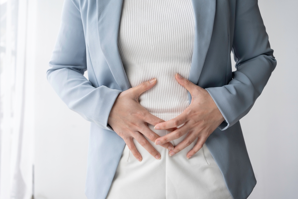 Businesswoman is standing in her office, holding her stomach in pain, possibly experiencing menstrual cramps or digestive problems
