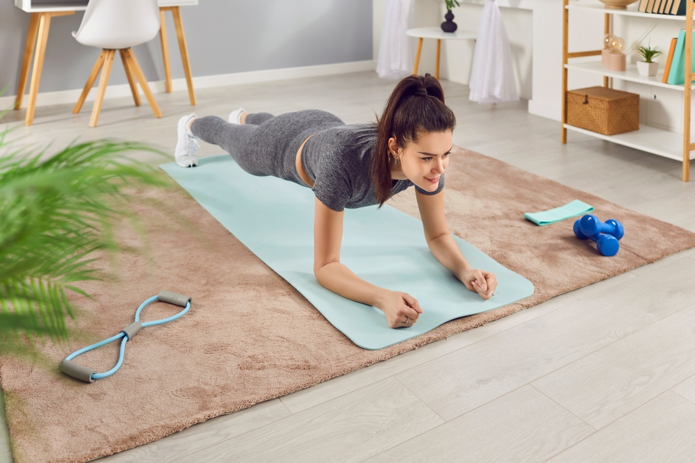 Woman is engaged in a workout session, doing a plank exercise as part of her fitness sport routine at home gym. This active training for core strength and stability, contributing to overall fitness.
