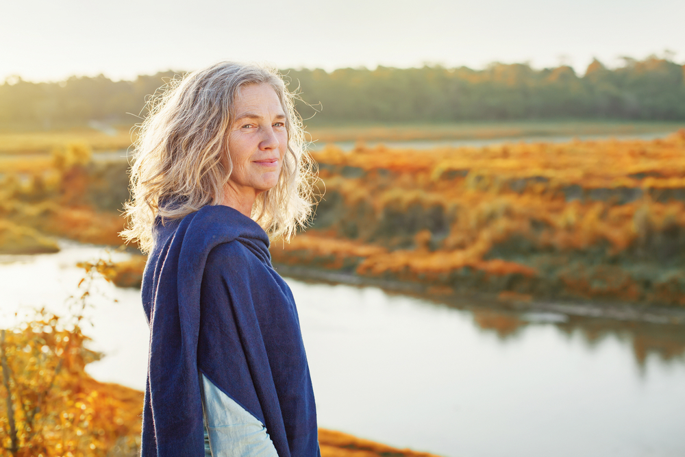 Beautiful mature woman standing in front of the river in autumn