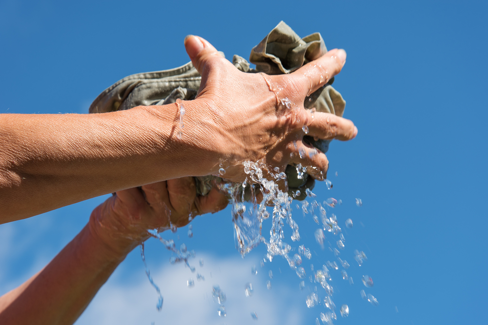 Hands squeeze wet fabric against blue sky.
