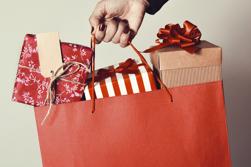 closeup of the hand of a young caucasian woman with her fingernails painted red holding a red shopping bag full of gifts wrapped in different papers