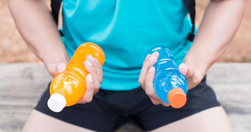 Bottle of energy drink and orange juice in hands of trail runner.