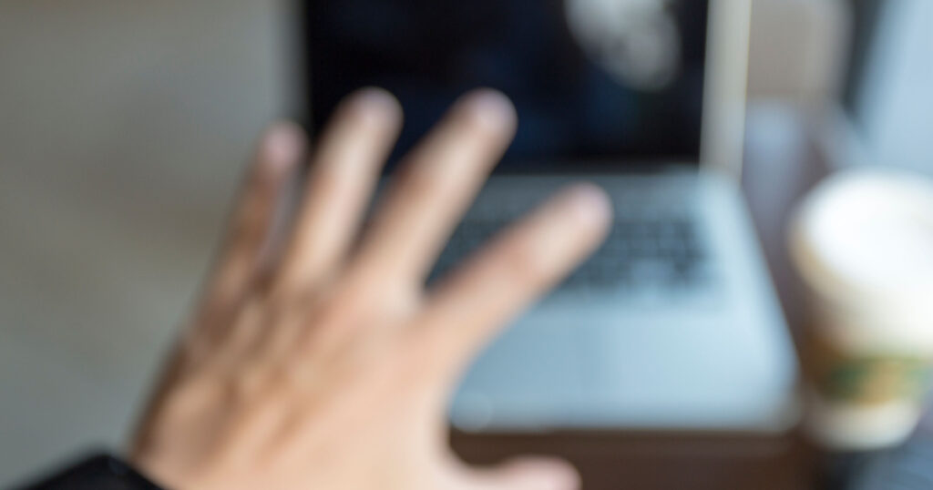 blurred vision of hand reached to laptop with coffee near window