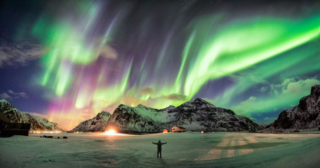 Aurora borealis (Northern lights) over mountain with one person at Skagsanden beach, Lofoten islands, Norway