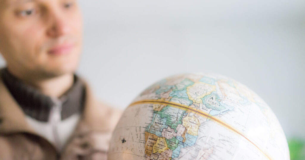 Young man holding looking at vintage retro old brown globe world map with equator, Africa continent