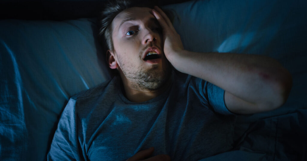 Top View of a Young Man in Bed at Night Having Terrible Nightmare, He Wakes Up Scared and Covered in Sweat.