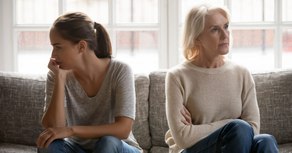 In quarrel elderly mother grown up daughter sit on couch separately having conflict, intergenerational misunderstanding, adult grandchild grandma difficult bad relations different generations concept