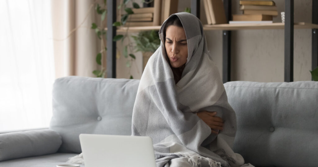 Sick ill young woman feel cold covered with blanket sit on sofa watching movie on laptop, annoyed girl shiver freezing warming at home wrapped with plaid, no central heating problem and flu concept