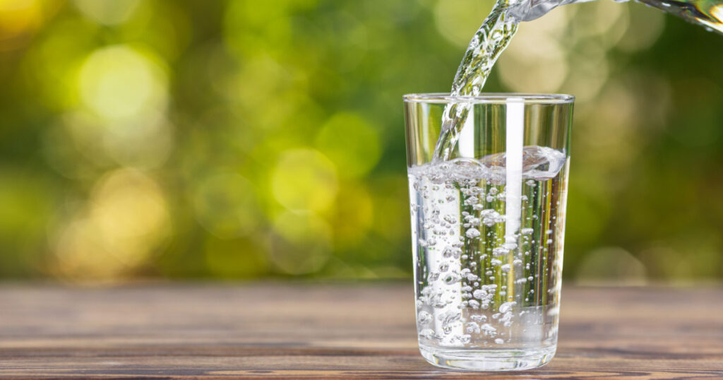 water from jug pouring into glass on wooden table outdoors