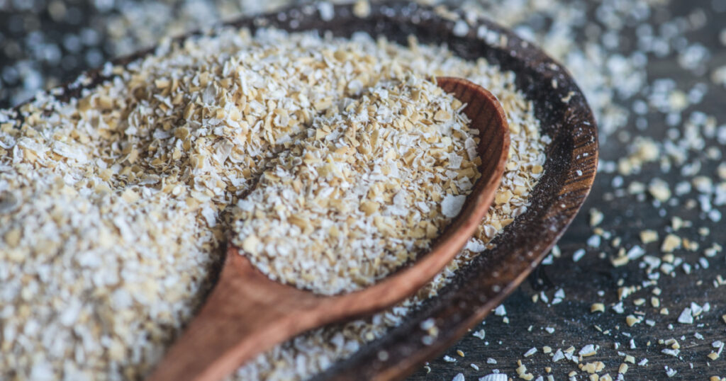 Healthy food concept with oats bran in a bowl with wooden spoon on dark rustic background with copyspace
