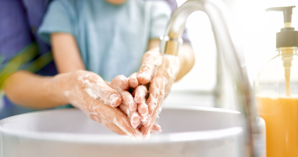 Kid and adult are washing their hands. Protection against infections and viruses. Close up.