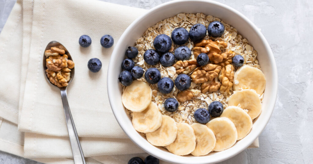 Oatmeal. Porridge with bananas, blueberries and walnut for healthy breakfast or lunch. Natural ingredients. Flat lay design on linen napkin and cement background