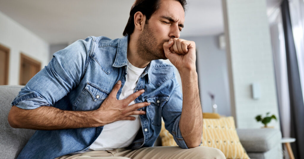 Sick man holding his chest in pain while coughing in the living room.
