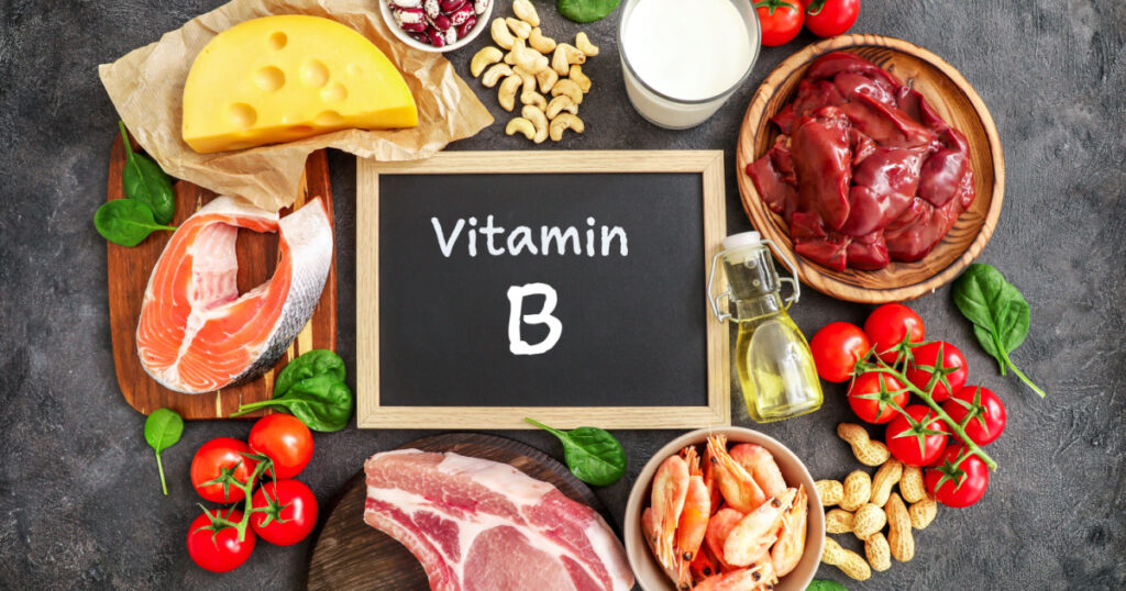 Assortment of high vitamin B sources on dark background: milk, liver, olive oil, tomatoes, prawns, peanuts, beef, spinach, salmon, keshew, cheese, haricot. Top view.
